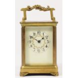 A brass carriage time piece, the off white dial with floral garland, ornate handle and feet, 11.5cm.