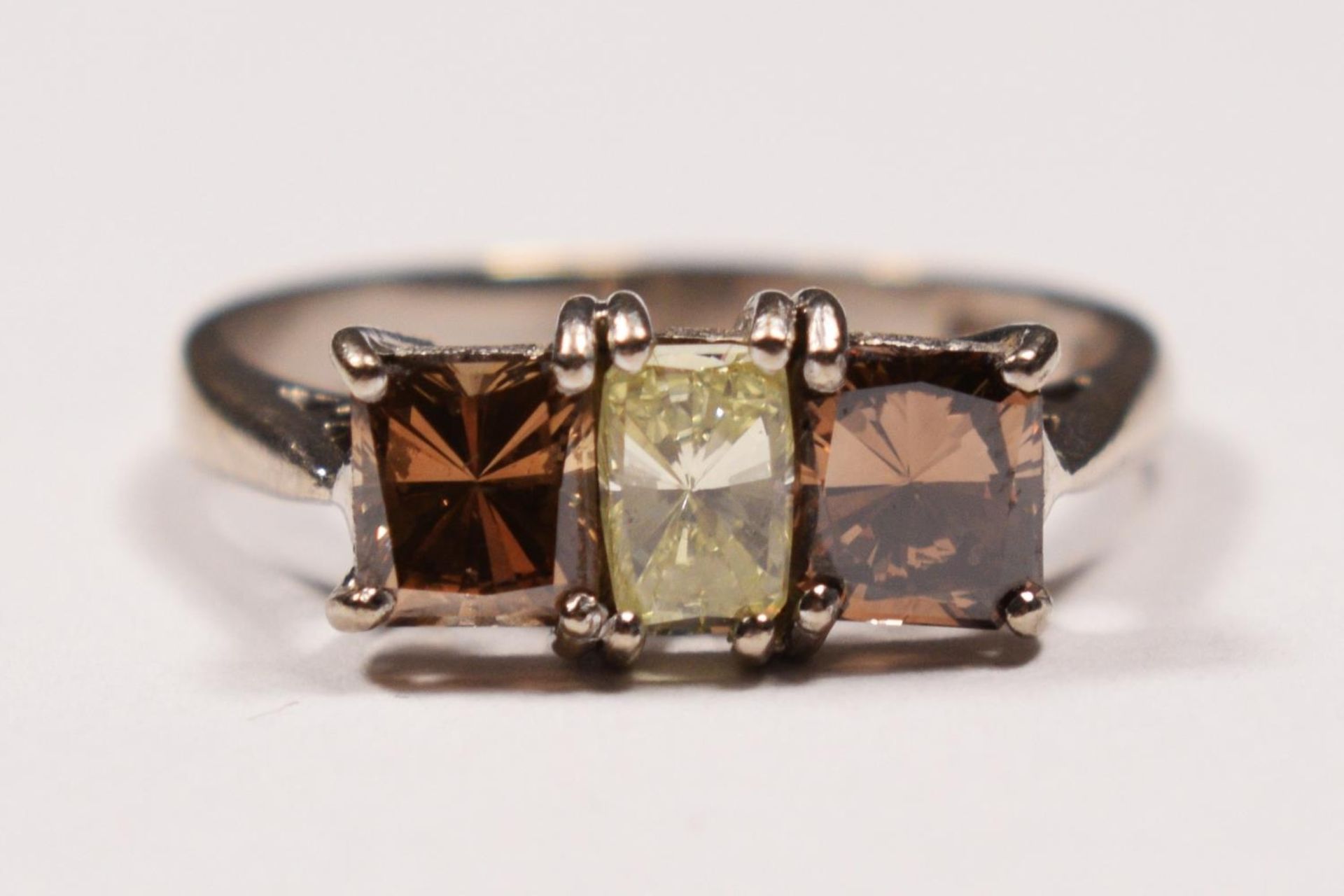 An 18ct white gold three stone diamond ring ring, claw set with a yellow stone of approximately 0.