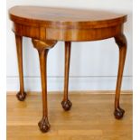 An Edwardian walnut demi-lune fold over games table with baize lined interior, raised on