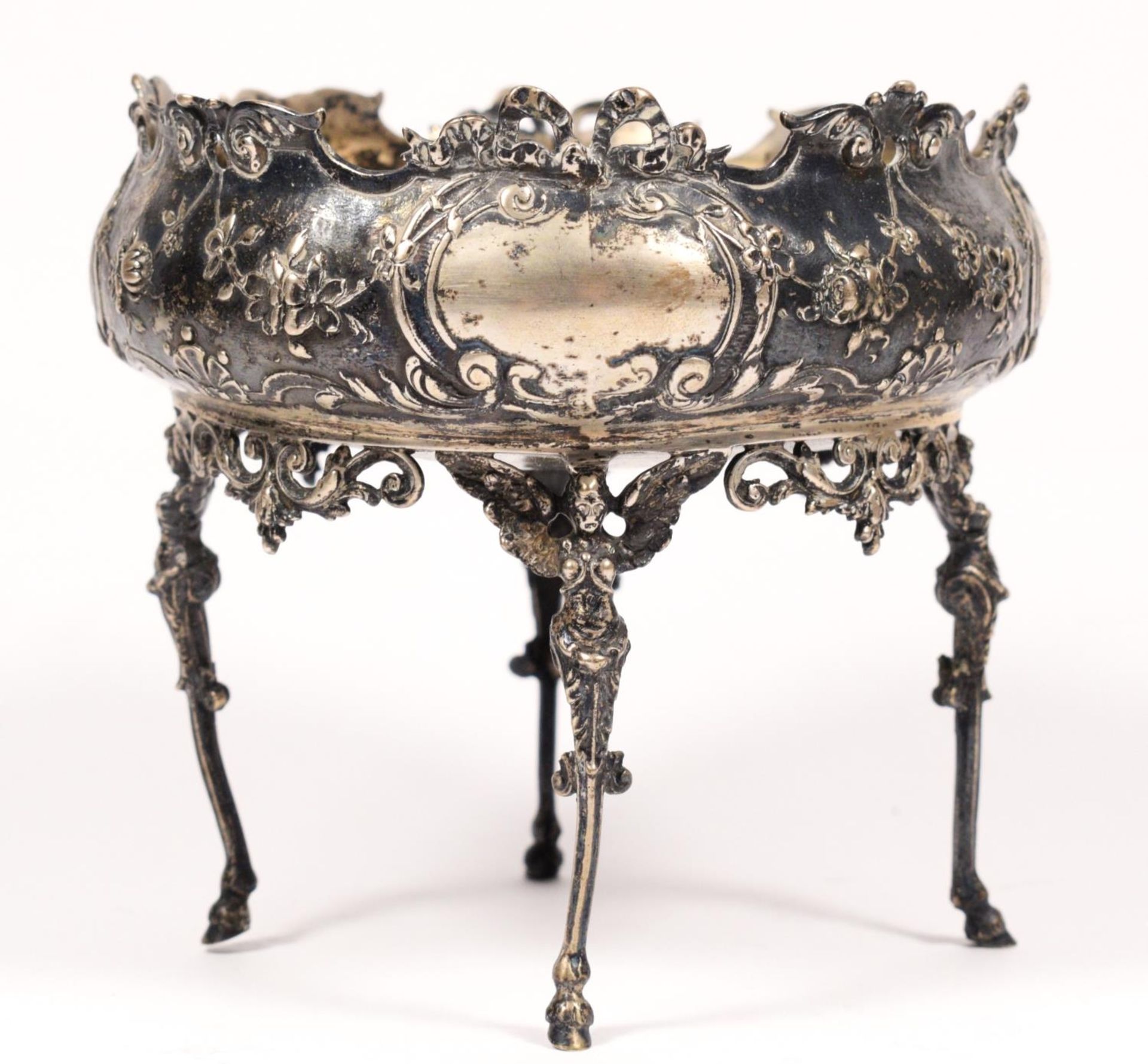 An early 20th century German bowl, with embossed decoration, raised on four winged angel legs,