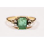 A 14K gold emerald and diamond ring, claw set with an emerald cut stone, 6 x 5mm flanked by single
