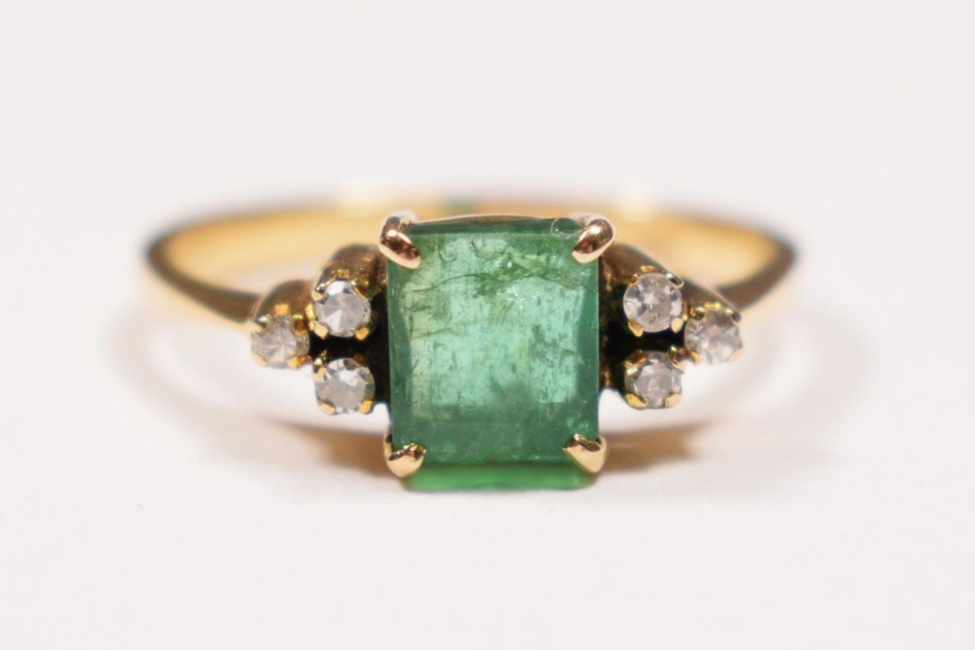 A 14K gold emerald and diamond ring, claw set with an emerald cut stone, 6 x 5mm flanked by single