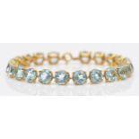 A gold and blue topaz line bracelet, claw set with brilliant cut stones, tested as 9ct gold,