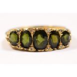 An 18ct gold five stone green tourmaline ring, carved claw set with mixed cut stones, diamond points