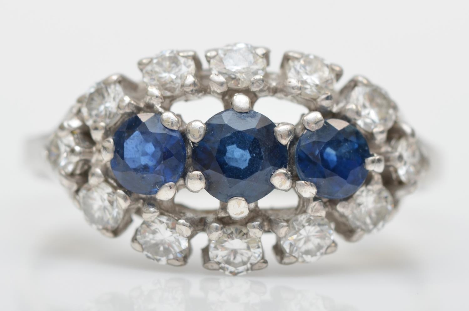 An unmarked 18ct white gold three sapphire and brilliant cut diamond cluster ring, diamond weight