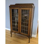 A leaded glass fronted display cabinet, decorated with carved floral pattern above two hinged doors,