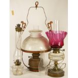 Three oil lamps, including one example with a cranberry glass flower shaped shade, converted to