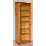 A pine Ducal opened fronted bookcase, five shelves over a lower shelf, arched top, on bun feet, 76 x