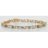 A 9ct gold diamond and blue topaz line bracelet, the oval mixed cut stone with two single cut