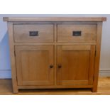 A modern light oak cabinet, having two deep drawers over two cupboard doors, opening to reveal a