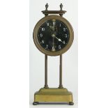 A British made brass gravity clock, the glass face with painted numerals, inside is a pendulum on