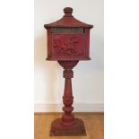 A cast iron free standing post/pillar box, painted red, raised on a pedestal with stepped base (