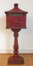 A cast iron free standing post/pillar box, painted red, raised on a pedestal with stepped base (