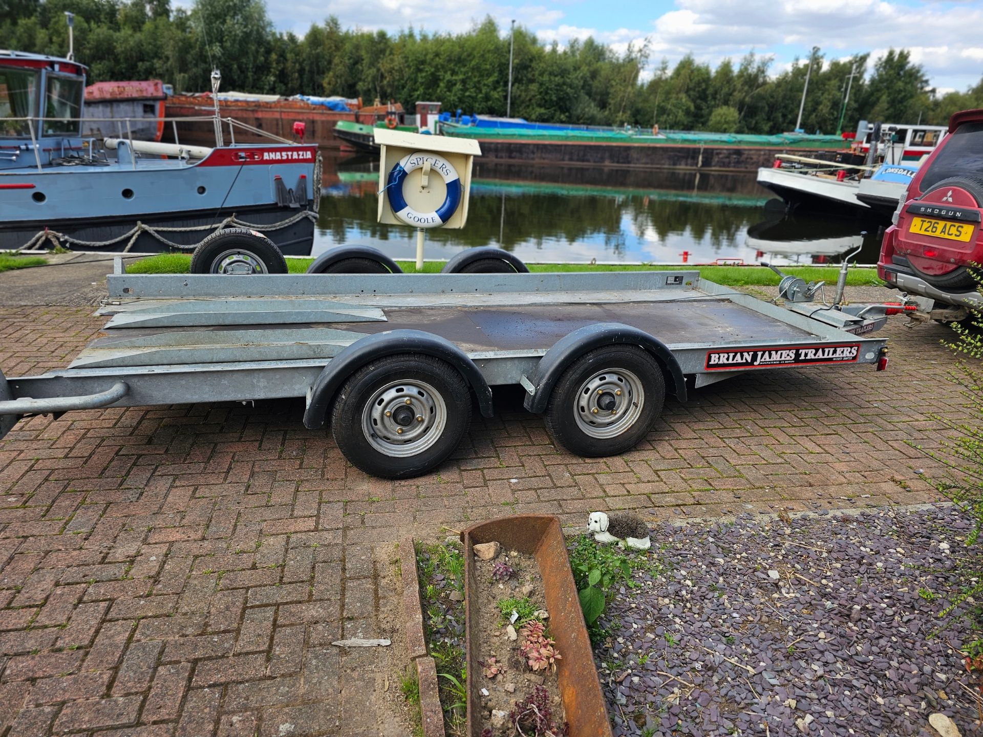 A Brian James, twin axle car trailer, up to 2700KG, with two ramps, manual winch and spare wheel.
