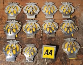A collection of eight AA bumper badges, a motorcycle AA badge and another example.