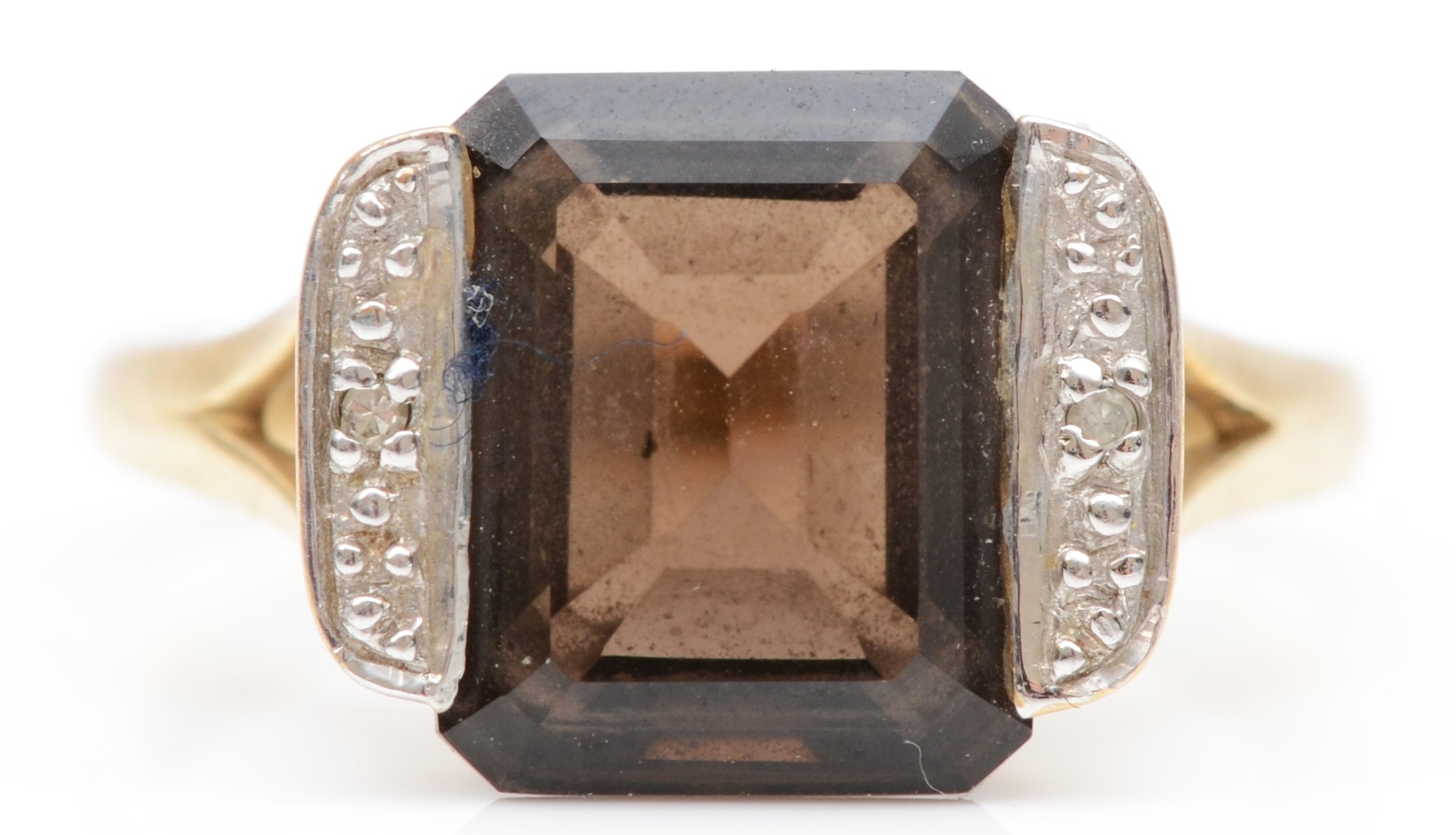 A 9ct gold emerald cut smokey quartz dress ring, the quartz flanked by two illusion set diamonds, P,