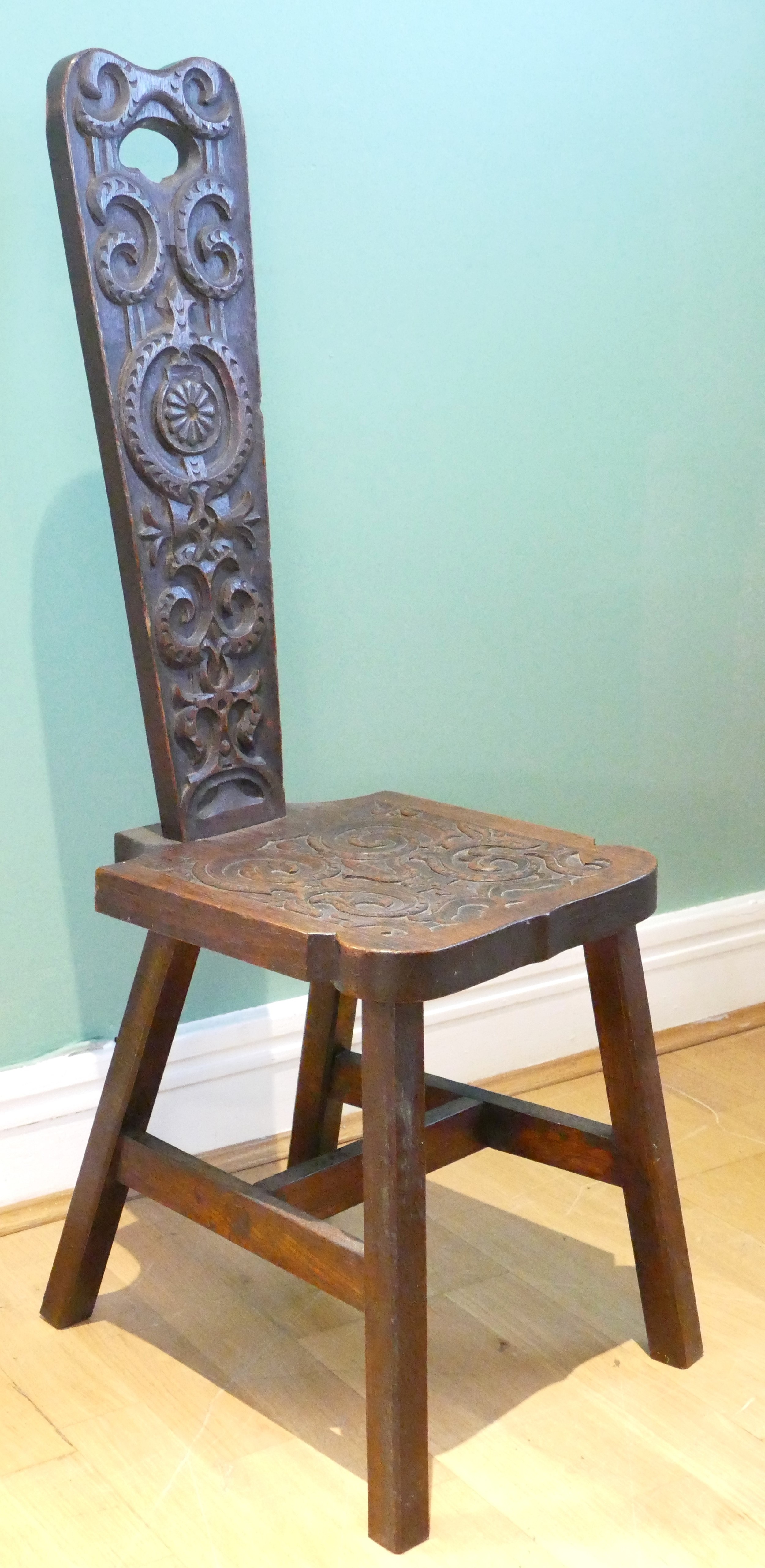 A late 19th century Welsh carved oak spinning chair, having carved floral decoration, raised on