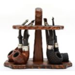 Six Petersen pipes, two with silver collars and a pipe stand