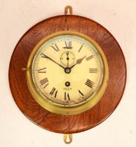 A Smiths Astral brass bulkhead clock, having 8 day movement, mounted on a mahogany backplate, 20cm