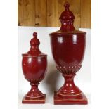 Two contemporary red painted urns and covers, each raised on square bases, together with a pair of