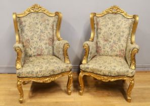 A pair of early 20th century gilt framed wing back arm chairs, raised on carved cabriole supports