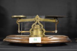 A set of brass postal scales, circa 1930s, with weights mounted on wooden plinth.