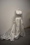 A mid to late 1950s wedding dress having bows to skirt and floral appliqué, long sleeves, scoop