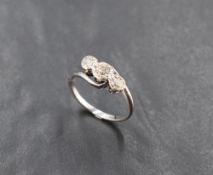 A white metal (thought to be 18ct gold) three stone diamond ring, the three illusion-set brilliant-