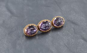A yellow metal (thought to be gold) and amethyst three stone brooch, having a linear arrangement
