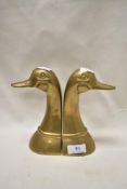 A pair of brass book ends in the form of ducks heads.