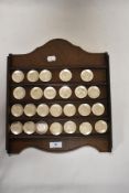 A wooden display rack housing a collection of embossed white metal miniature floral plates.