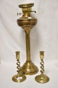 A Victorian brass column paraffin lamp, void of chimney, and two twist stem candlesticks.