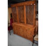 A reproduction yew wood bookcase having astral glazed display section over triple drawer and