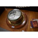 A porthole style brass clock mounted on mahogany plinth