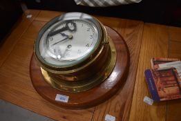 A porthole style brass clock mounted on mahogany plinth