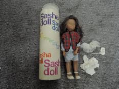 A 1960's original Sasha Doll wearing vest, blue and white chequered dress and shorts, tartan coat