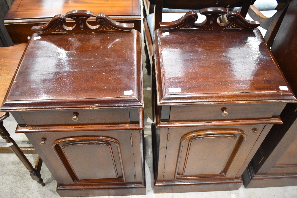 A pair of reproduction stained mahogany bedside cabinets, having short swan-neck raised backs over