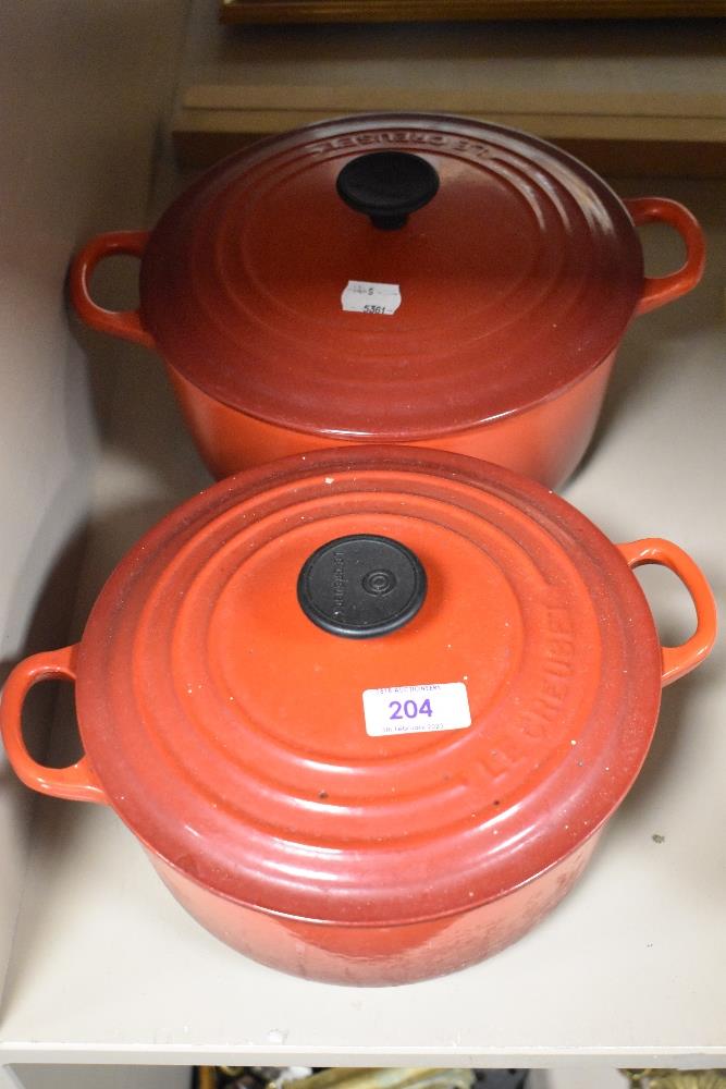 Two Le Creuset casserole dishes in red enamel, both used but in good condition.