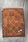A vintage hand woven Afghan wool rug in red and brown grounds with a floral pattern with fringing