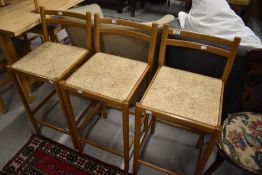 Three modern stained frame bar stools having rail backs and seagrass seats