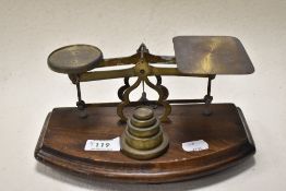 A set of brass postal scales, circa 1930s, with weights mounted on wooden plinth.