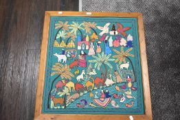 A large ethnic style needle work, having animals, people, trees and houses depicted throughout on