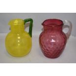 A hand blown lemonade jug in yellow glass with green handle and a similar water jug in dimpled