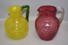 A hand blown lemonade jug in yellow glass with green handle and a similar water jug in dimpled