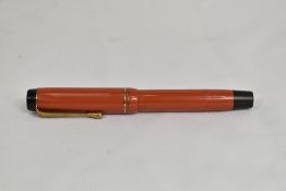 A Parker Duofold Streamlined button fill fountain pen in coral red with two bands to cap bearing the