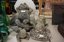 Three concrete garden ornaments in the form of frogs.
