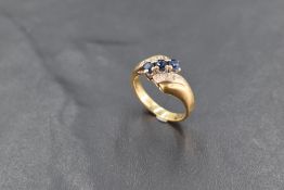 A yellow metal, sapphire and diamond dress ring, having three central sapphires within bands of