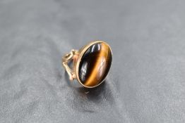 An oval tigers eye cabouchon stone ring having a diagonal set collared mount to open shoulders on