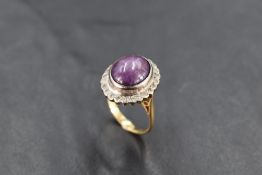 An Amethyst star oval cabochon ring having a diamond chip surround on a yellow metal loop stamped