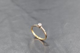 A diamond solitaire ring, approx 0.128ct in a claw set mount to moulded shoulders on a yellow